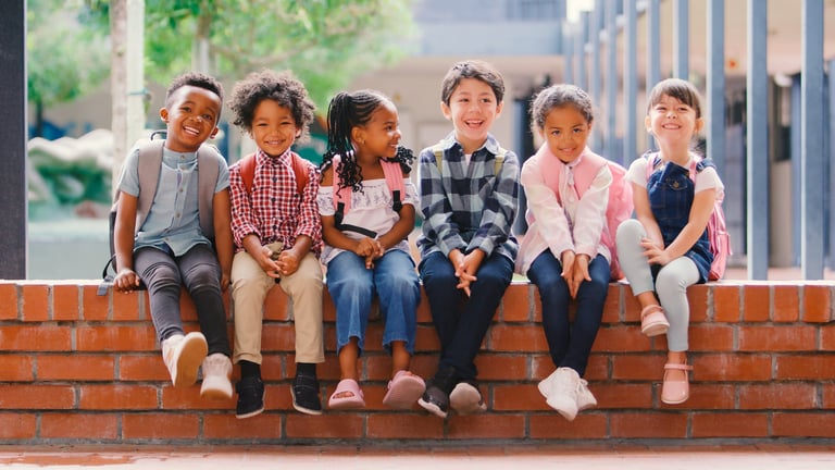 Fröhliche Grundschulkinder lächeln gemeinsam draußen vor der Schule